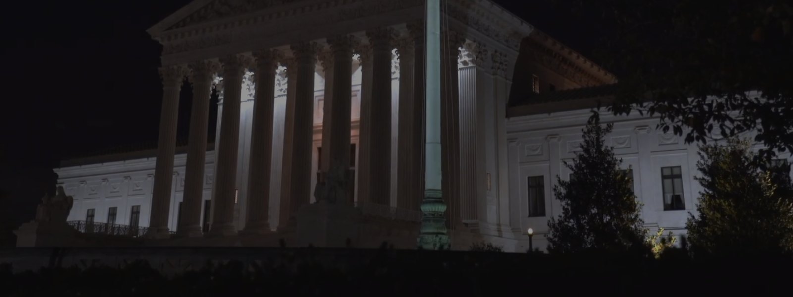The courthouse at night, columns lit, flag in front